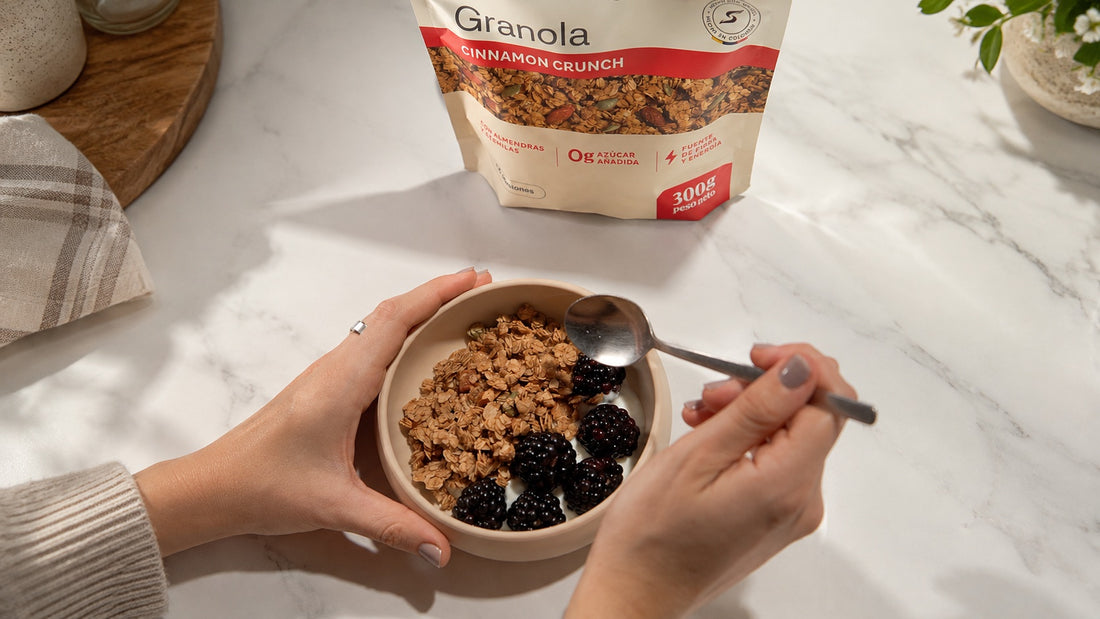 Manos sosteniendo un bowl de yogur griego con zarzamoras y granola Cinnamon Crunch, con la bolsa de Con Sentido al fondo